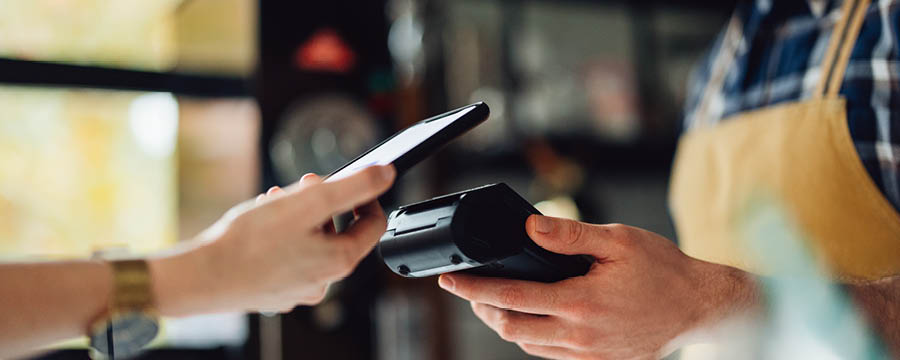 Shopper places their smartphone on a card machine to pay for a purchase.