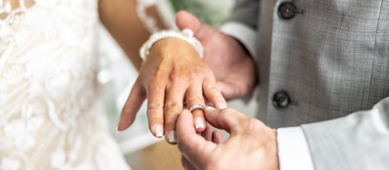 Groom putting wedding band on bride's finger.