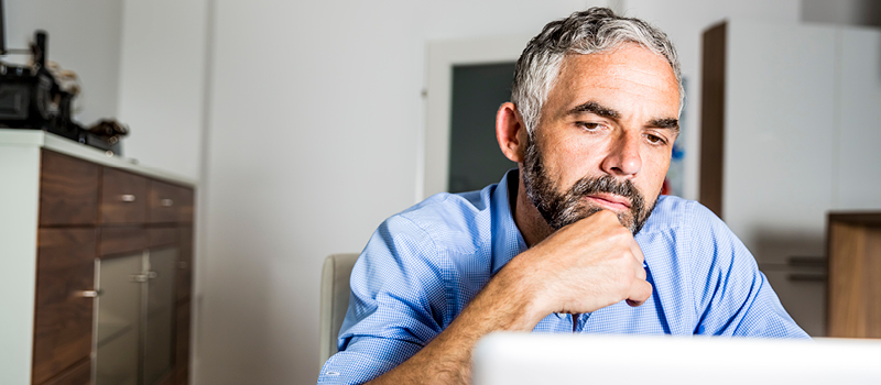 Man in his home office contemplating a question while looking at his computer